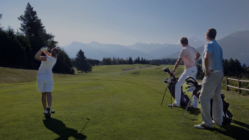 Foto: Golferin beim Abschlag auf dem Golfplatz Crans-Montana im Wallis, dahinter die Walliser Alpen